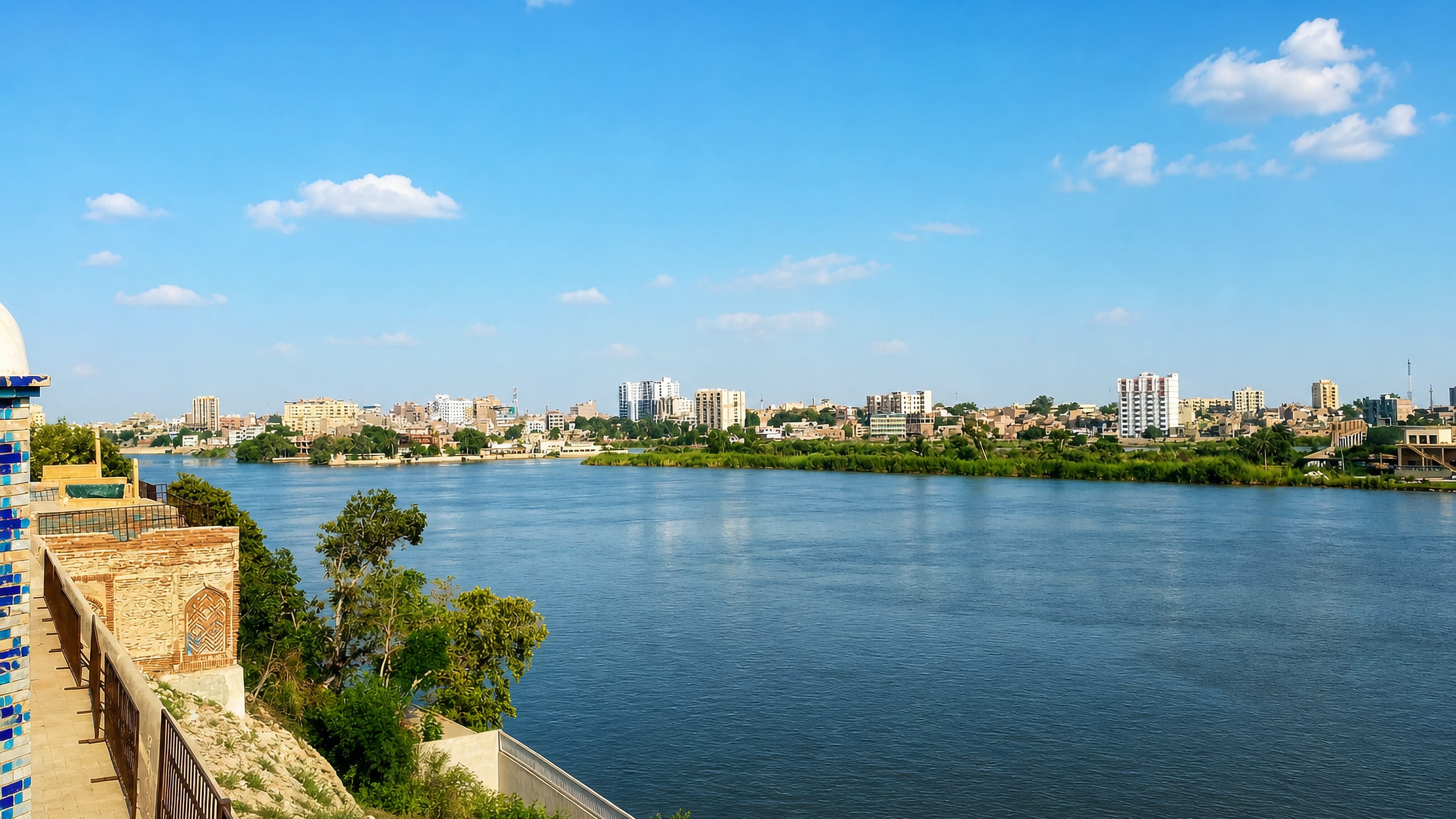 The Indus River at Sukkur seen from a tiled riverside shrine, with the city's low skyline opposite