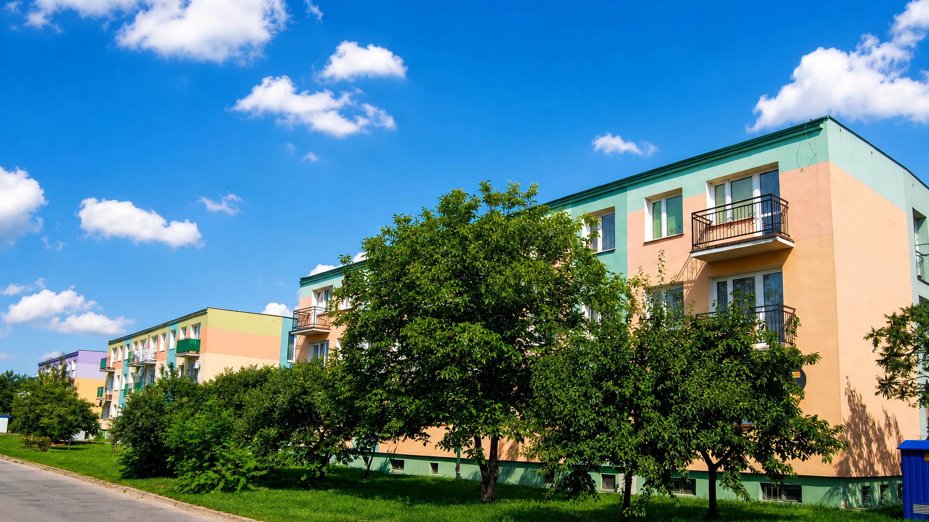 Pastel low-rise apartment blocks behind fruit trees on a quiet street in Dziekanka, Gniezno