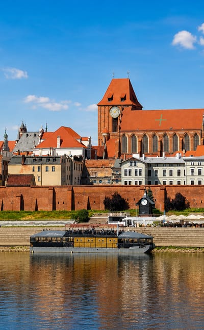 Toruń's medieval Old Town of red-brick Gothic churches and riverside walls seen across the Vistula River.