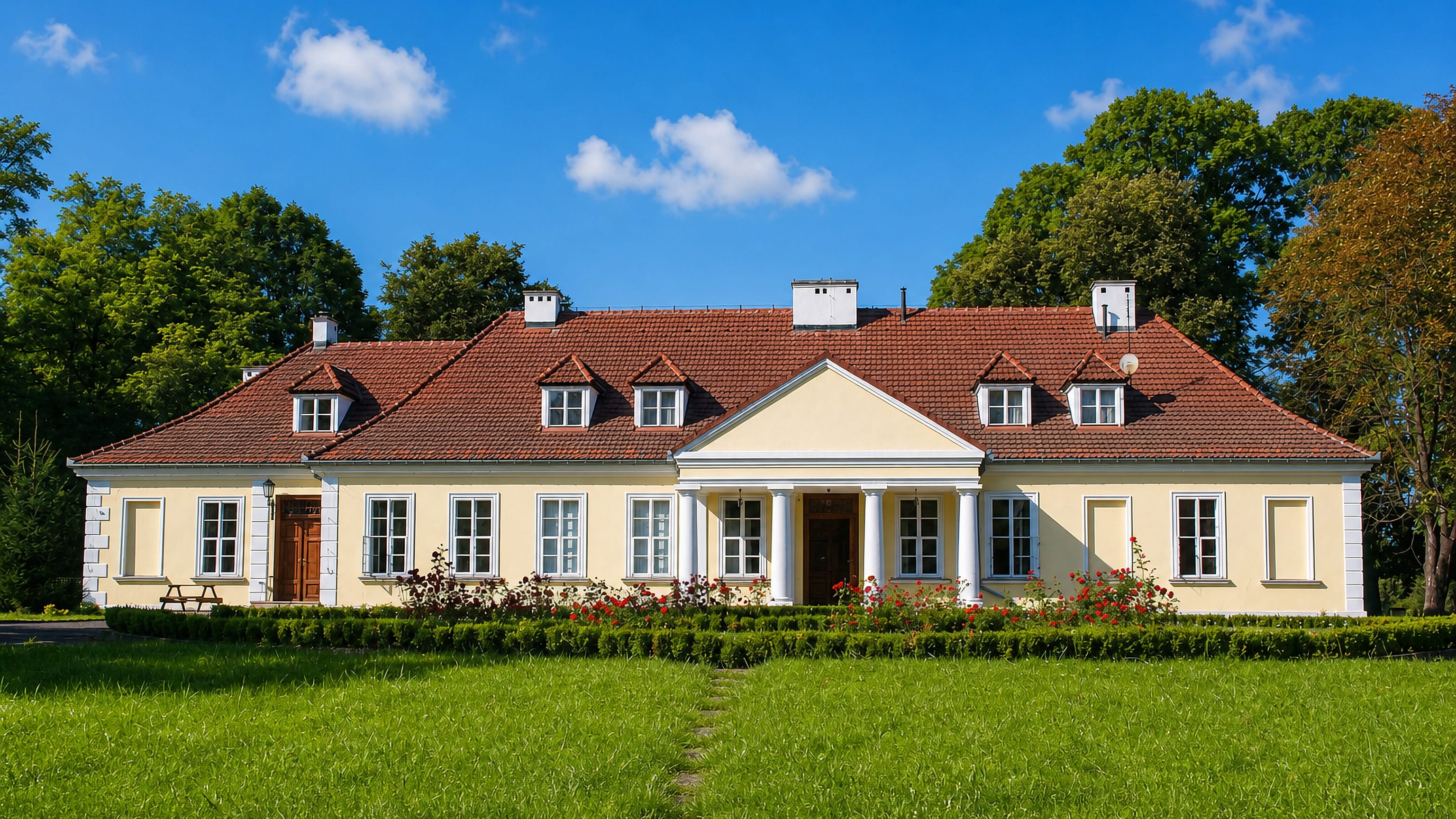 Cream-rendered Polish manor house with a columned portico and clipped hedges on a lawn in Branice.