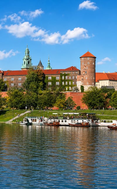 Krakow's Wawel Castle on its hill above the Vistula river with tour boats moored below the red-roofed complex