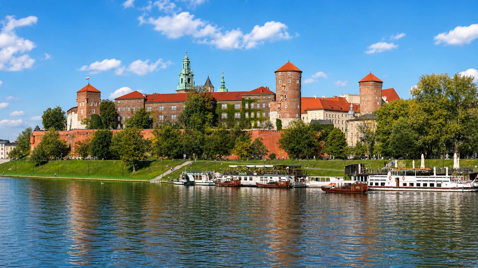 Krakow's Wawel Castle on its hill above the Vistula river with tour boats moored below the red-roofed complex