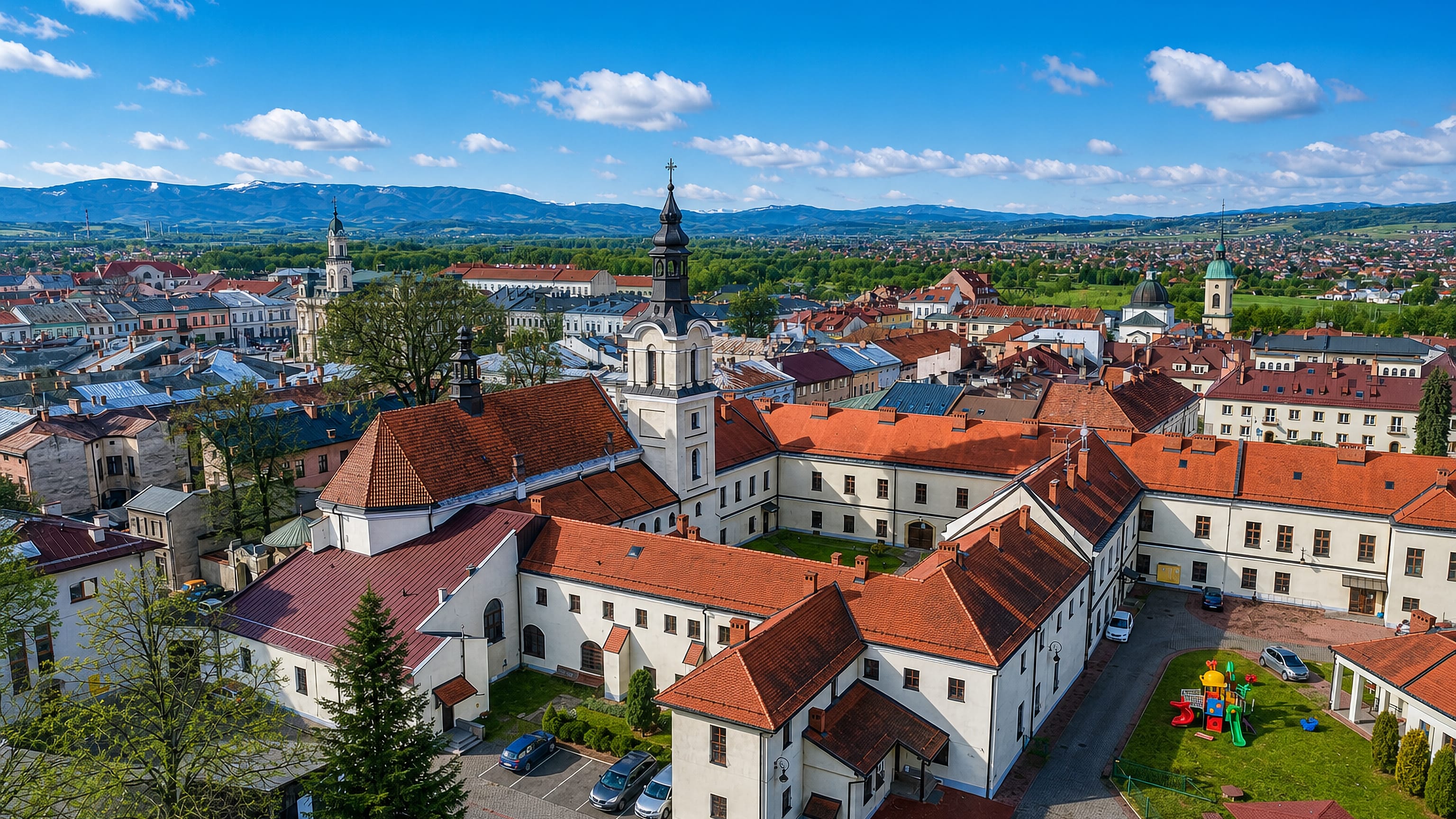 Red-tiled roofs and baroque church towers of Nowy Sącz old town, Poland, with the Beskid mountains behind.