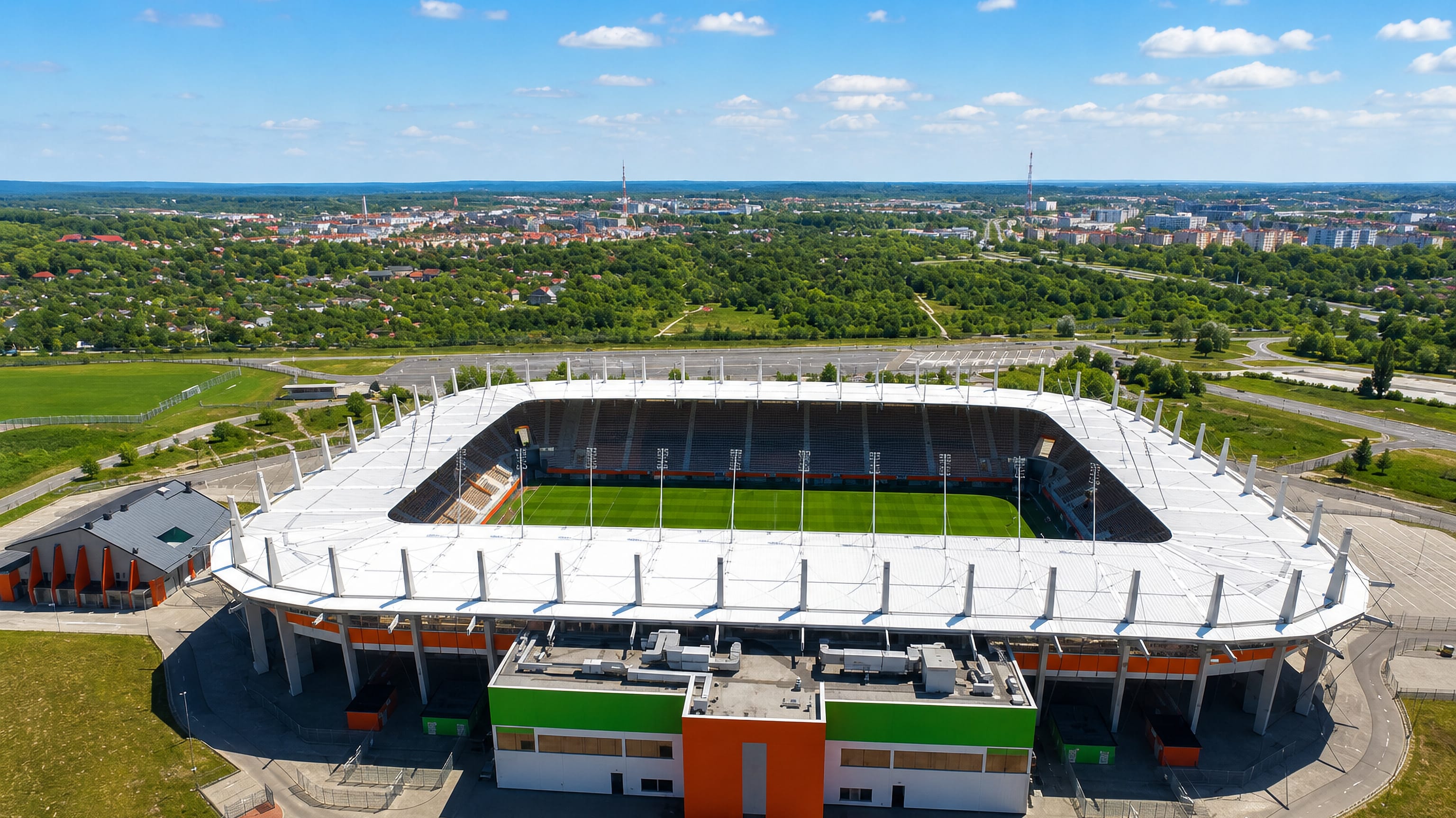 Aerial view of Lubin's orange-and-green football stadium with the town and Lower Silesian countryside behind.