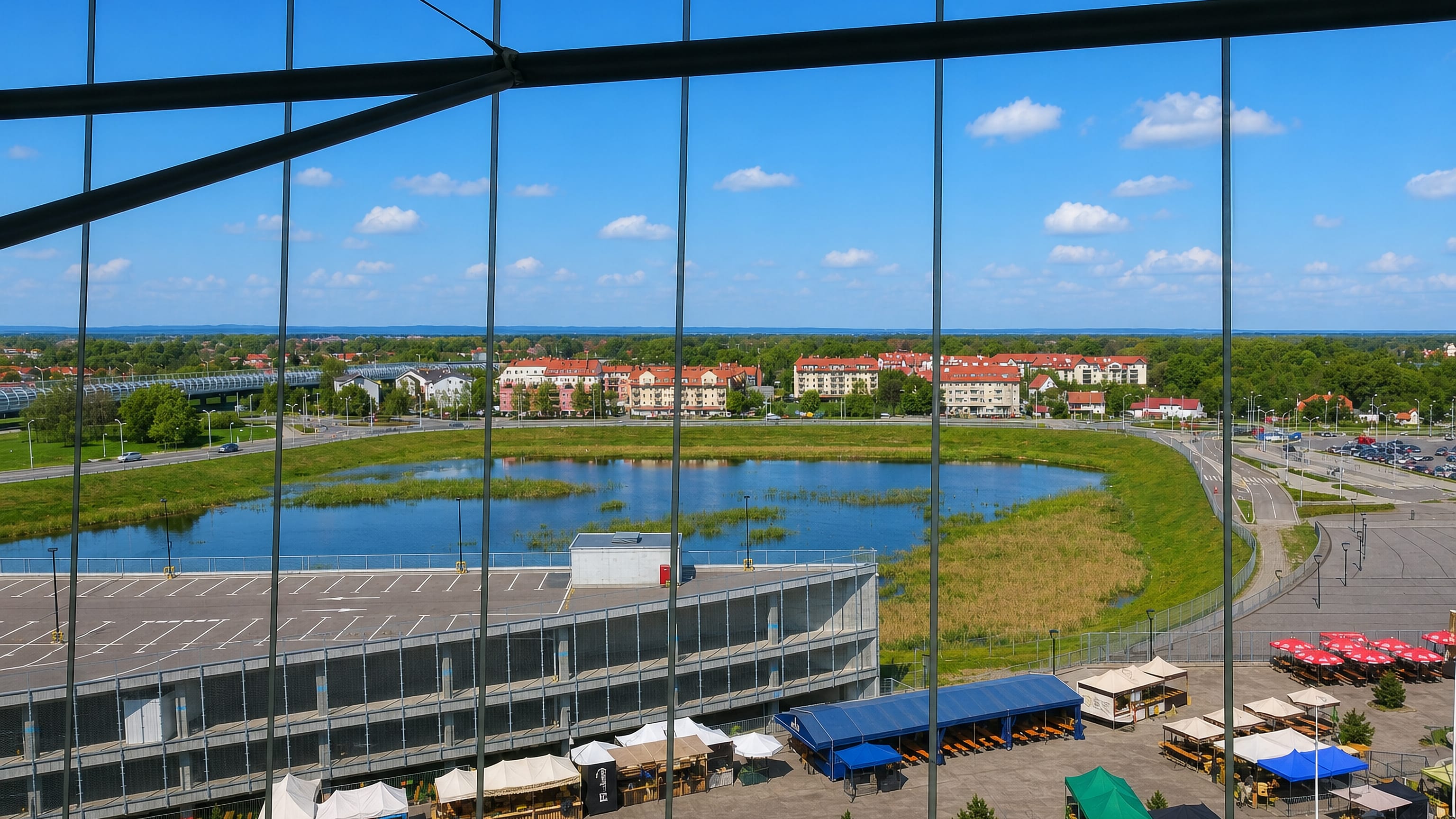 View over Pilczyce in Wroclaw from behind a glass facade, across a retention pond, car park and market stalls