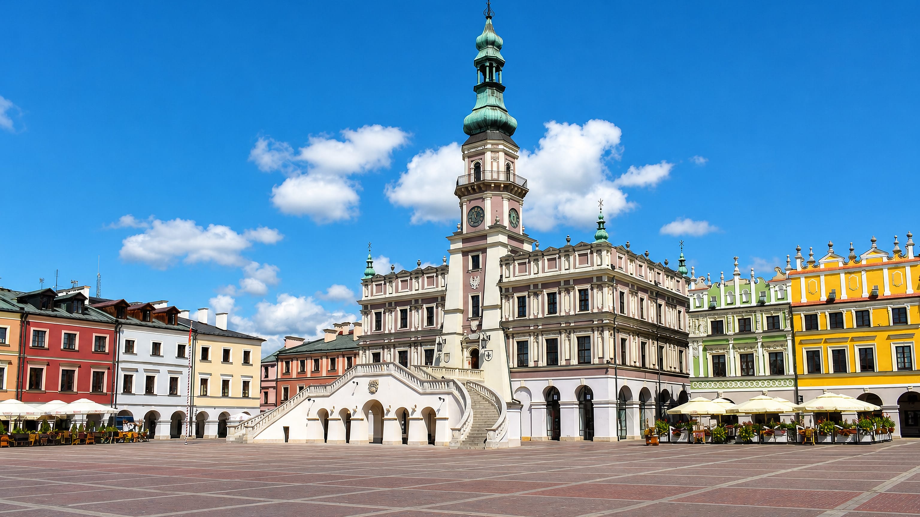 Zamość's Great Market Square in daylight, with the Renaissance town hall, fan staircase and colourful arcaded townhouses.