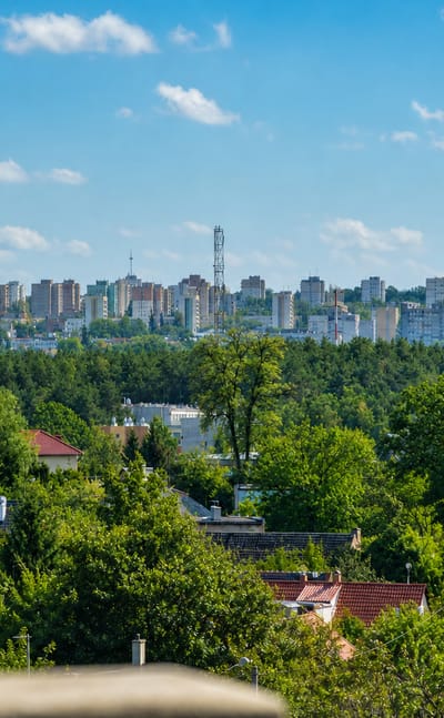 Zielona Góra skyline of apartment blocks along a ridge above a broad belt of green forest and rooftops.
