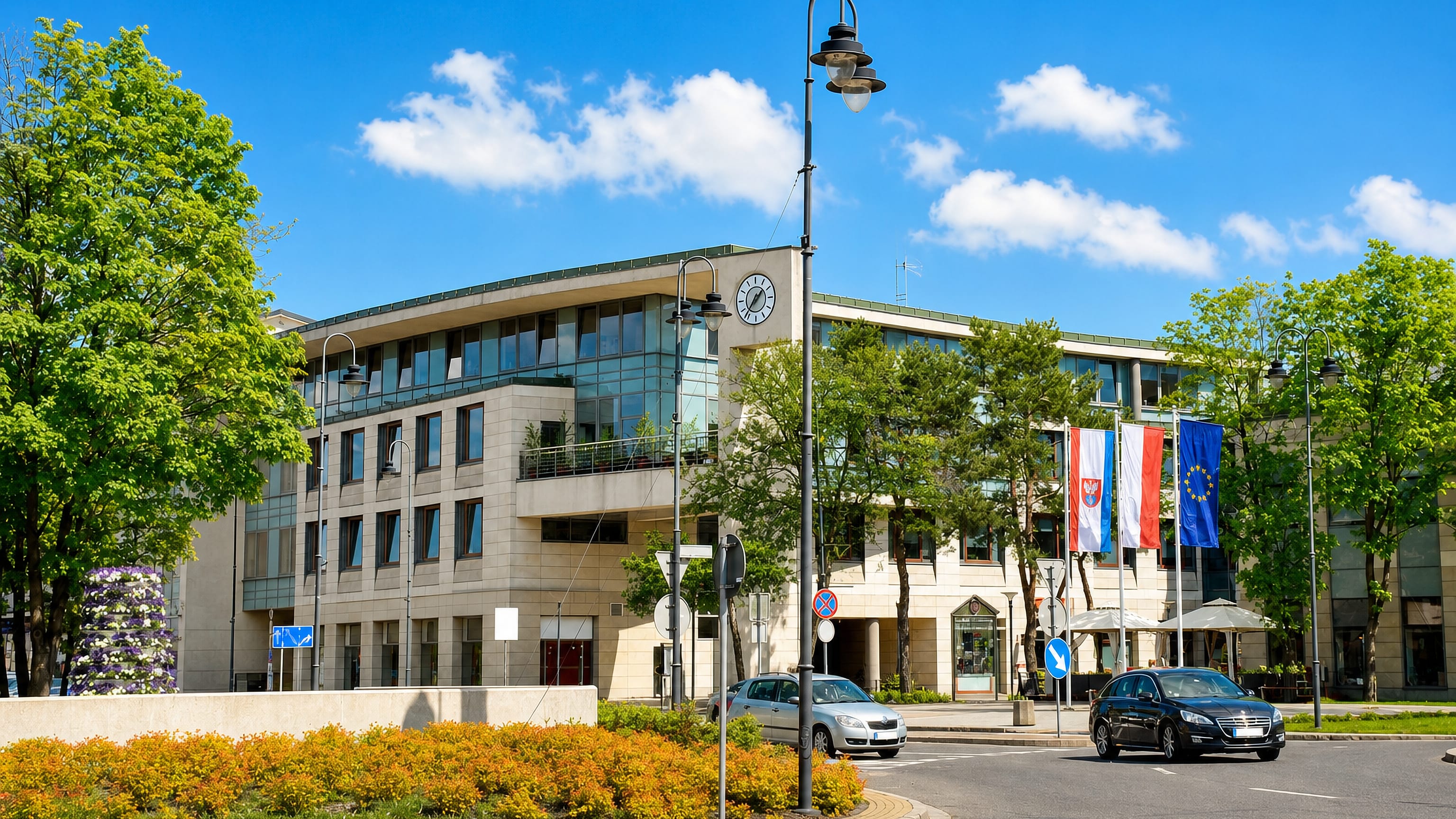 Modern civic building with a clock and Polish and EU flags beside a landscaped roundabout in Legionowo, Poland
