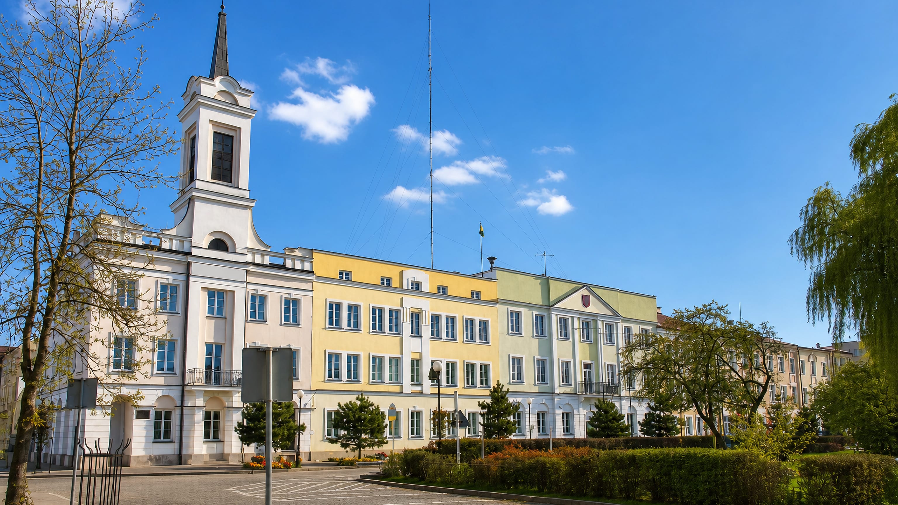 Ostroleka town hall in Poland, its white tower and pastel wings facing the paved square on a spring day.