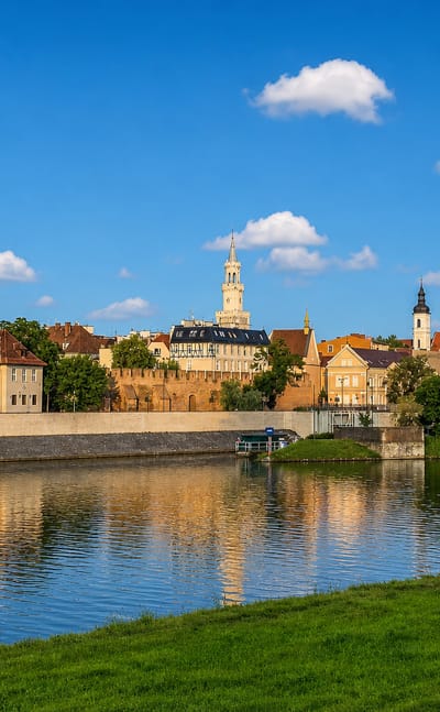 Opole waterfront across the Oder, with the cathedral's twin brick spires and town hall tower reflected in the river.