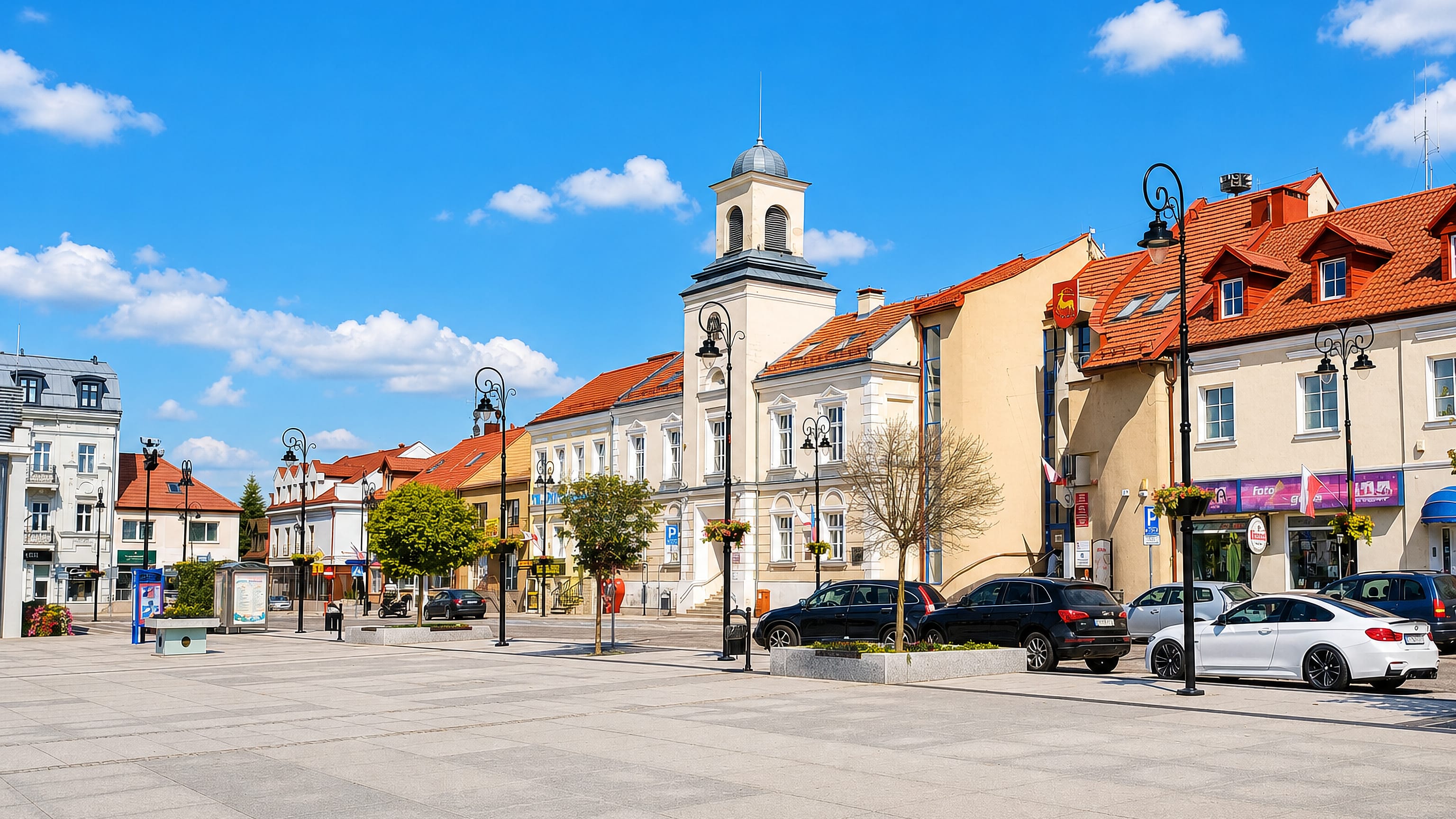 Łomża's broad paved market square in Poland, lined with pastel townhouses and a white town hall tower.