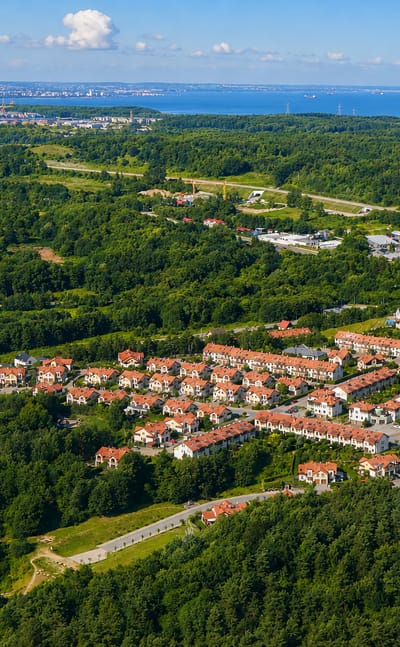 Aerial of red-roofed housing among forest with the Bay of Gdansk beyond in the Bretowo district.