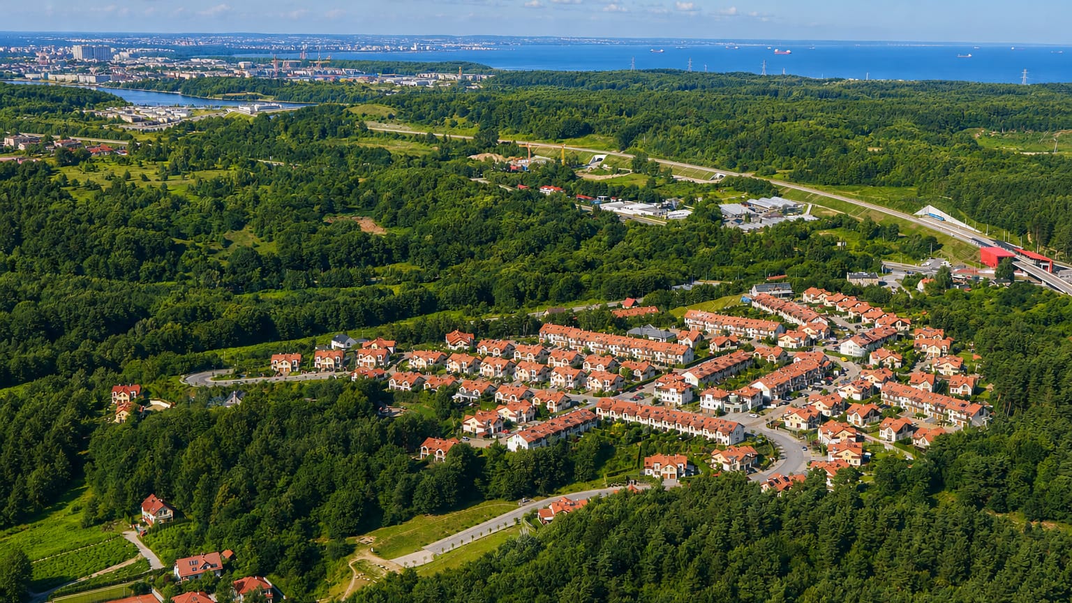 Aerial of red-roofed housing among forest with the Bay of Gdansk beyond in the Bretowo district.
