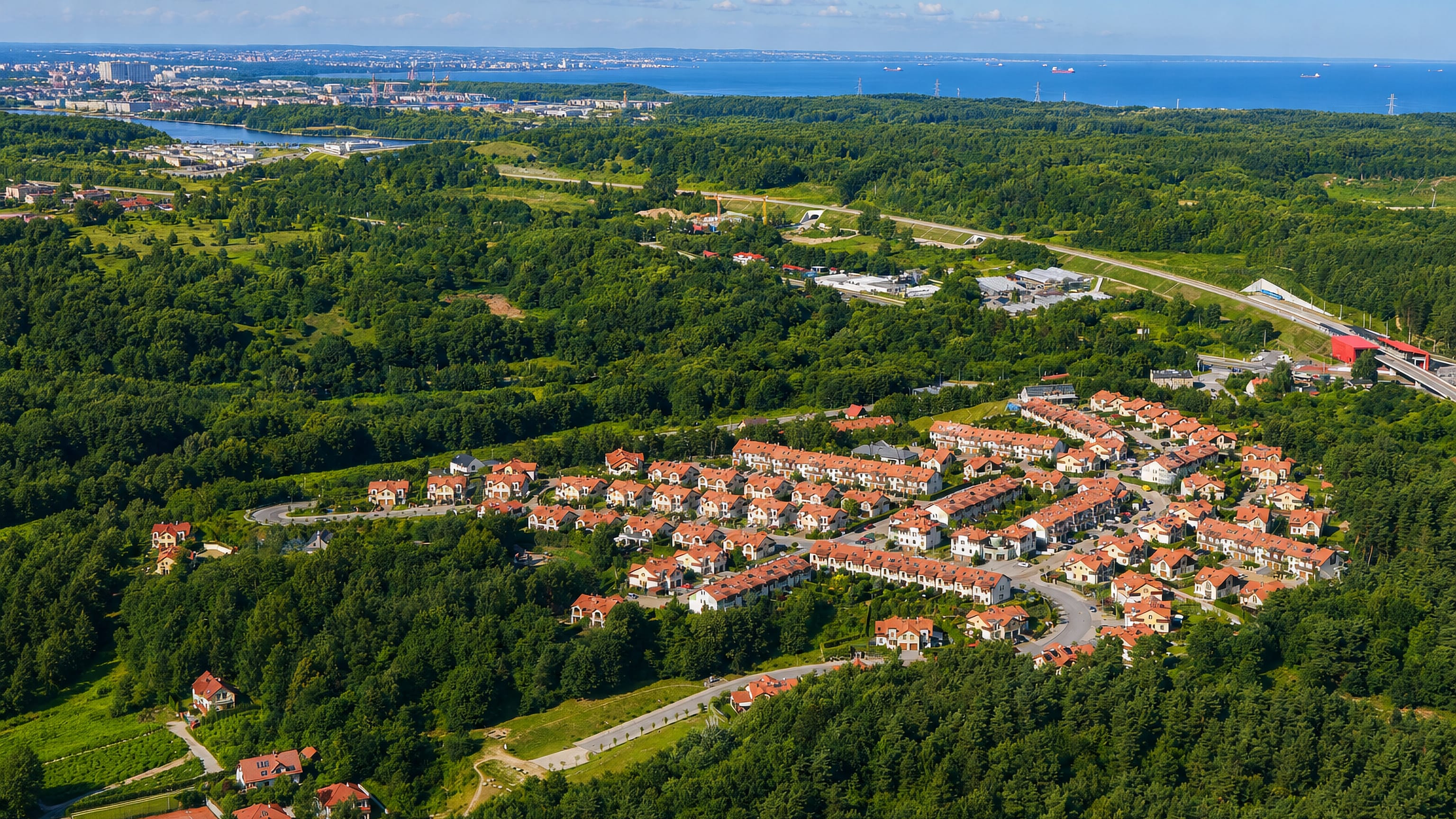 Aerial of red-roofed housing among forest with the Bay of Gdansk beyond in the Bretowo district.