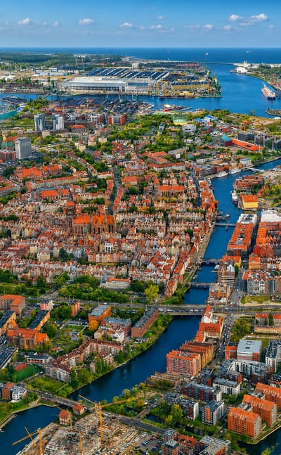 Aerial view of Gdańsk Old Town with red-roofed Main Town, the Motława river and the shipyard port on the Baltic beyond.