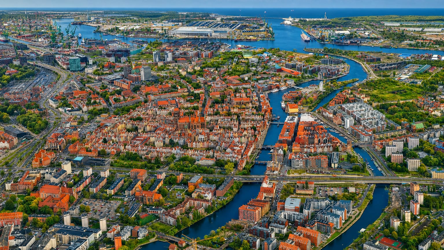 Aerial view of Gdańsk Old Town with red-roofed Main Town, the Motława river and the shipyard port on the Baltic beyond.