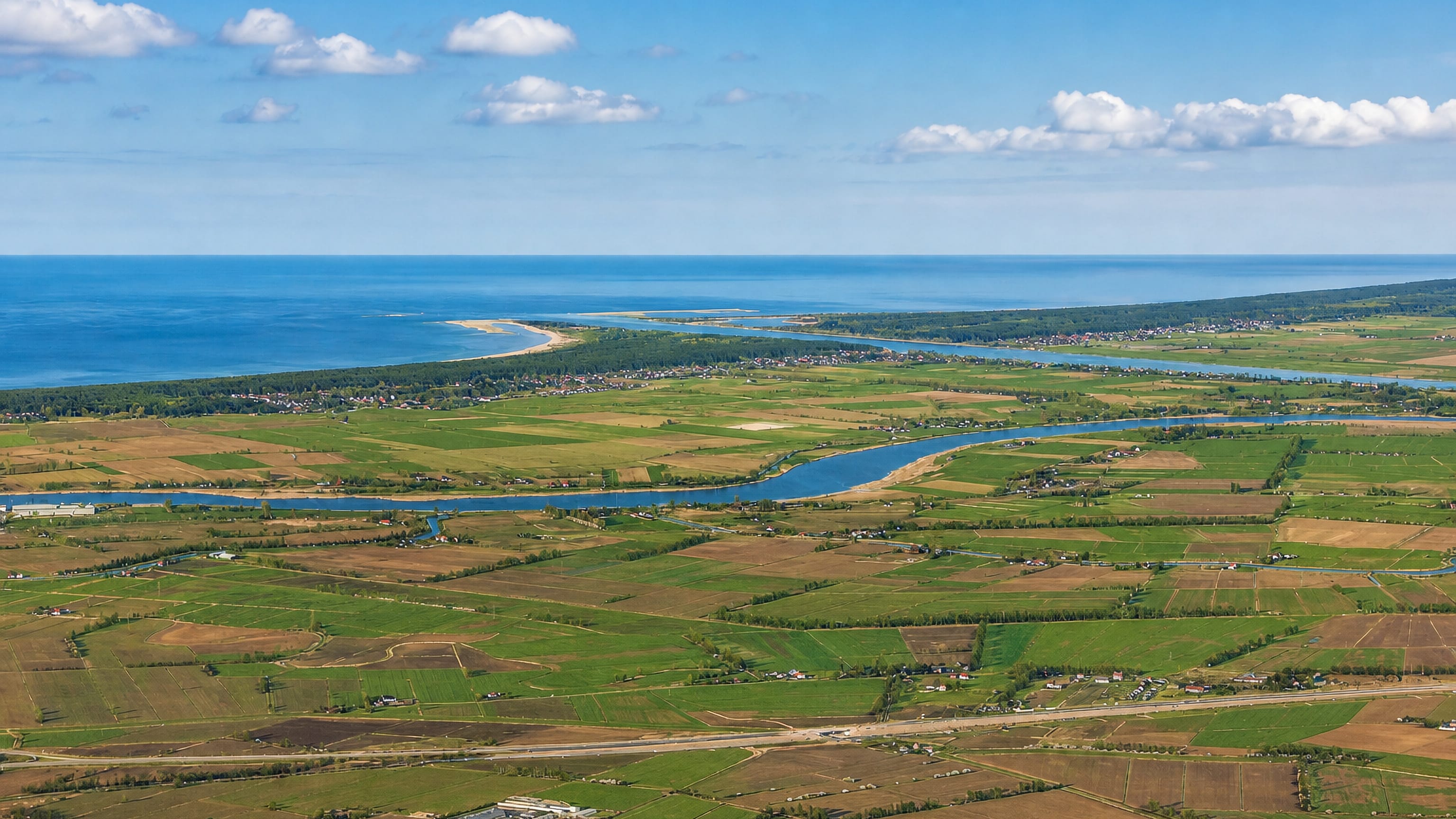 Aerial over Sobieszewo island near Gdansk, with delta farmland, the Vistula channel and the Baltic coast.