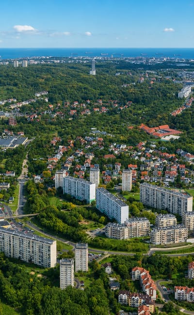Aerial over the green Suchanino district of Gdańsk with apartment blocks and houses, the Baltic port on the far horizon.