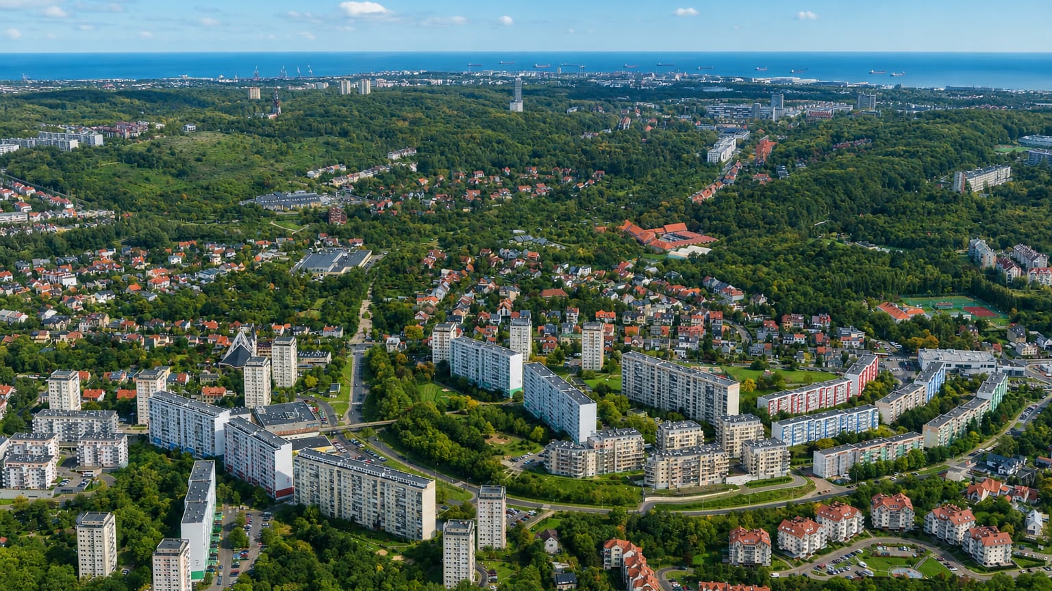 Aerial over the green Suchanino district of Gdańsk with apartment blocks and houses, the Baltic port on the far horizon.
