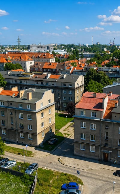 Wrzeszcz Dolny rooftops in Gdansk with the amber Arena Gdansk stadium and shipyard cranes on the horizon.
