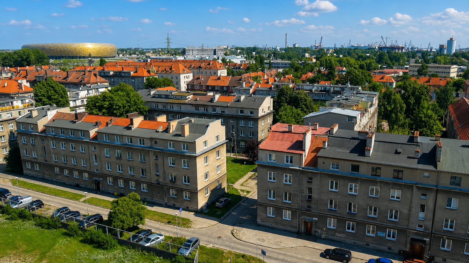 Wrzeszcz Dolny rooftops in Gdansk with the amber Arena Gdansk stadium and shipyard cranes on the horizon.