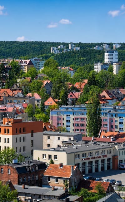 Colourful low-rise buildings and red roofs of the Wrzeszcz Gorny district of Gdansk with wooded hills behind.