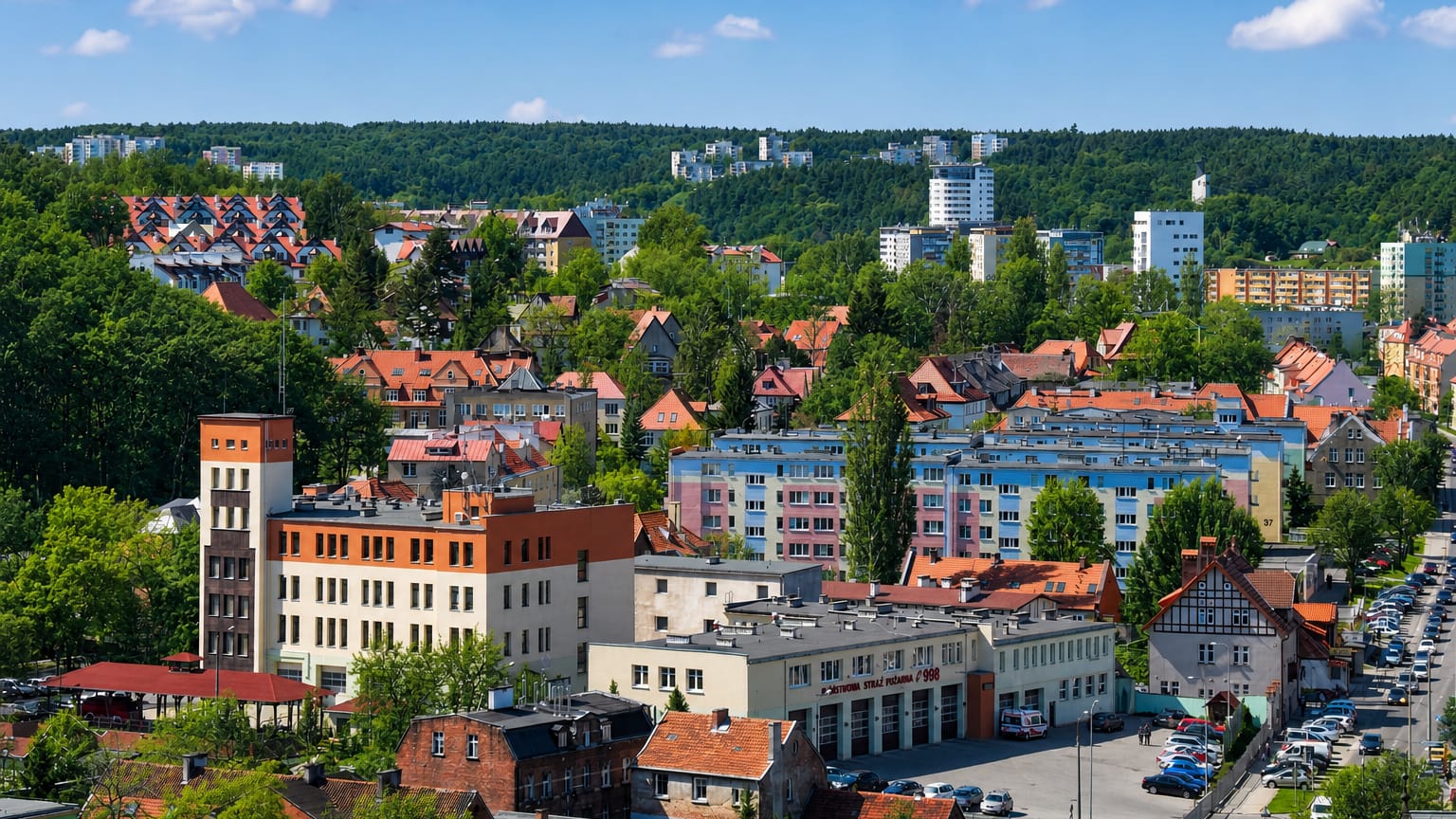 Colourful low-rise buildings and red roofs of the Wrzeszcz Gorny district of Gdansk with wooded hills behind.