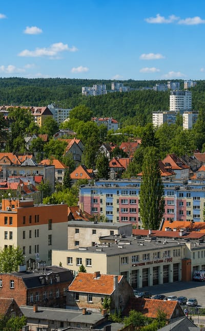 Elevated view over the Wrzeszcz district of Gdańsk with mid-rise apartment blocks, red-roofed houses and wooded hills beyond.