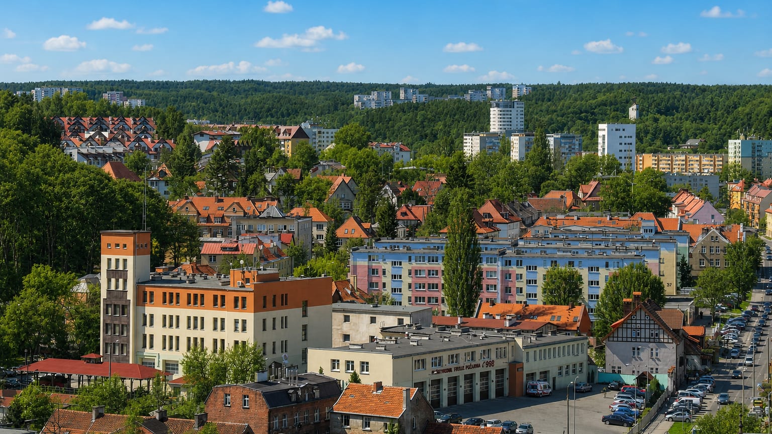 Elevated view over the Wrzeszcz district of Gdańsk with mid-rise apartment blocks, red-roofed houses and wooded hills beyond.