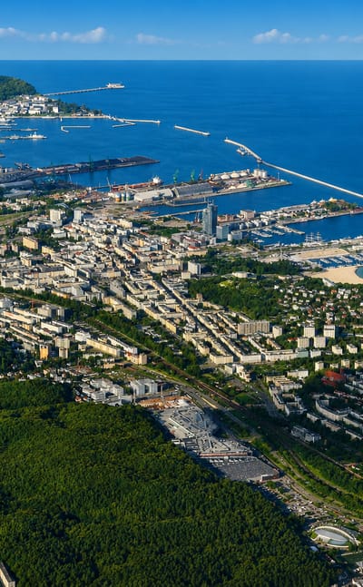 Aerial view of Gdynia's Baltic port, marina and downtown along the coast with forested hills and ships at sea.