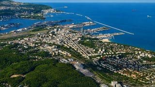 Aerial view of Gdynia's Baltic port, marina and downtown along the coast with forested hills and ships at sea.