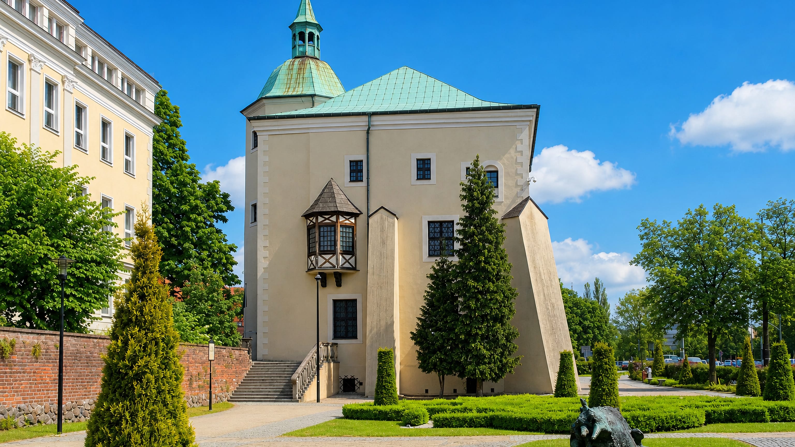 The Castle of the Pomeranian Dukes in Słupsk, its green copper tower and timbered oriel above trimmed lawns
