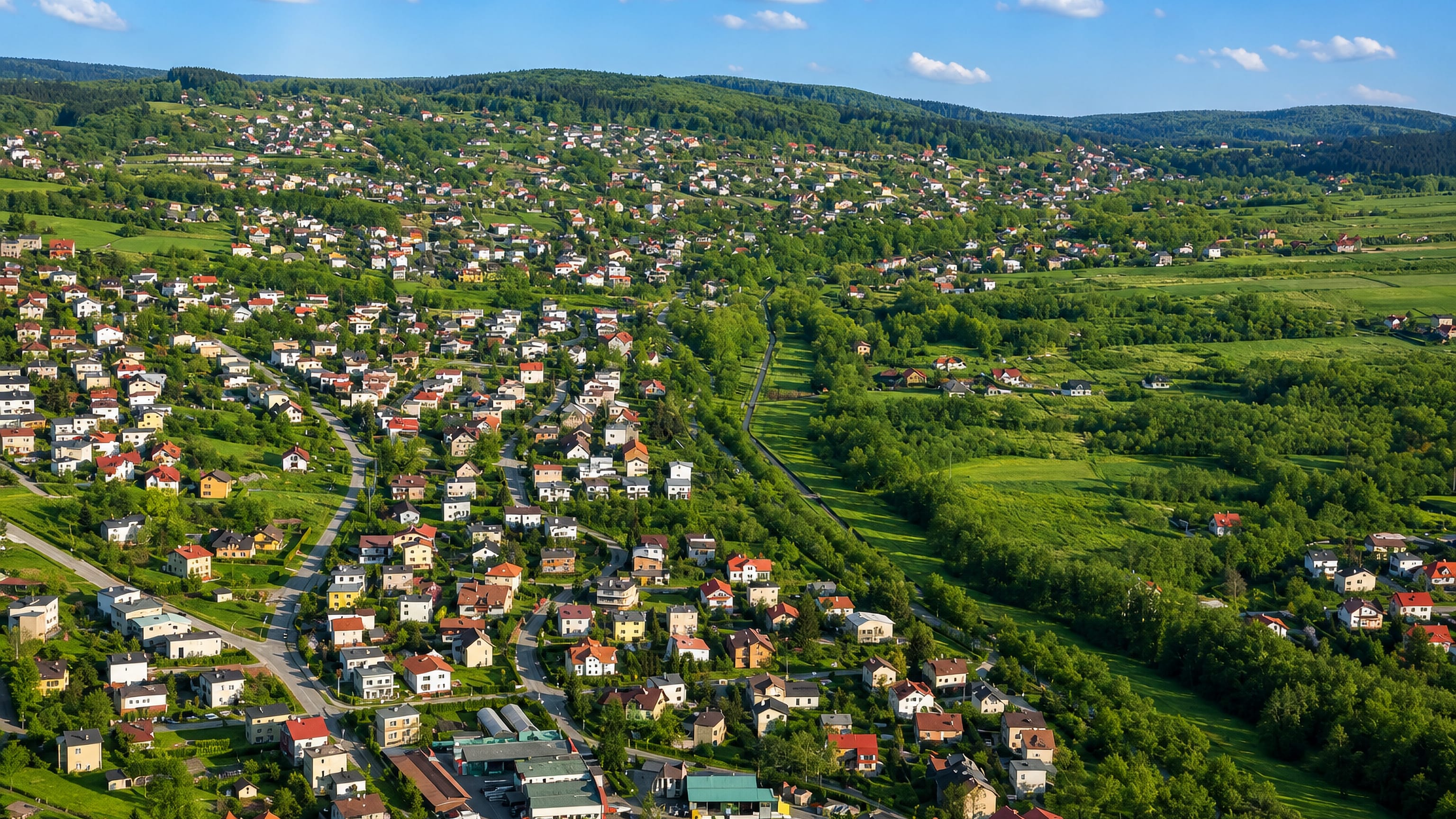Aerial view of Straconka in Bielsko-Biała, houses scattered up wooded Beskid hillsides above green meadows.