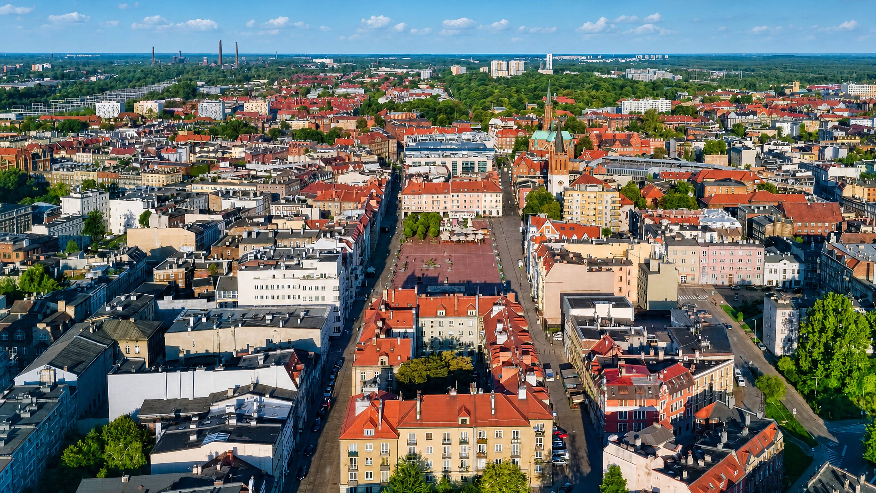 Aerial view over Bytom's red-roofed tenement blocks and brick church spire, with Silesian chimneys beyond, Poland