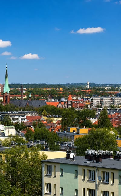 Gliwice townscape with a green church spire and a lattice radio tower rising above rooftops under a blue sky.
