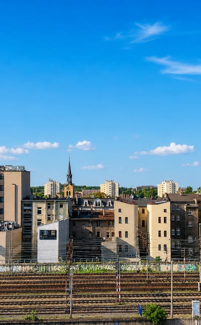 Katowice skyline in daylight above wide railway yards, with a modern tower, church spire and tenement rooftops.