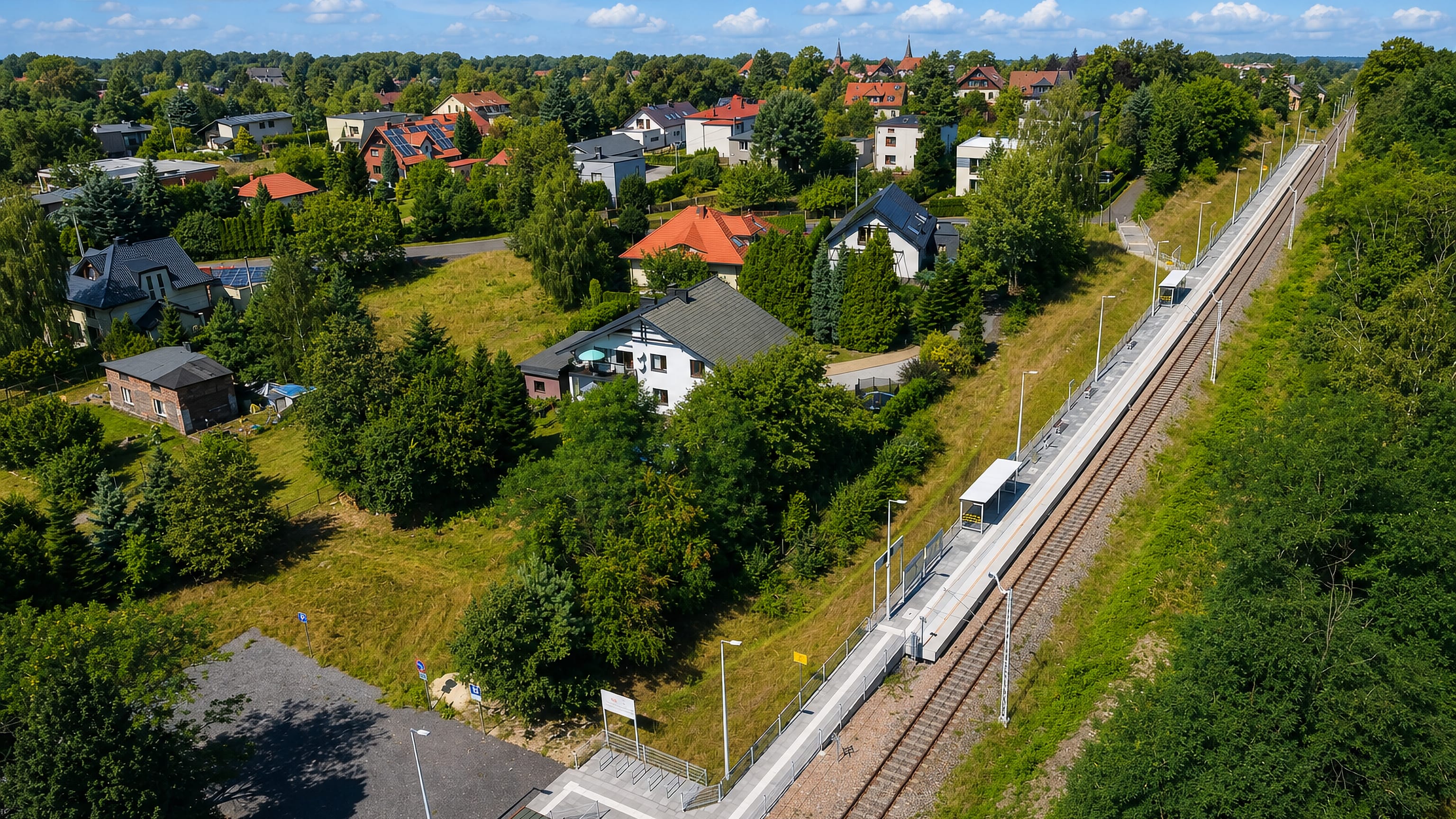 Aerial view of Podlesie in Katowice, with detached houses and gardens beside the railway line and platform.