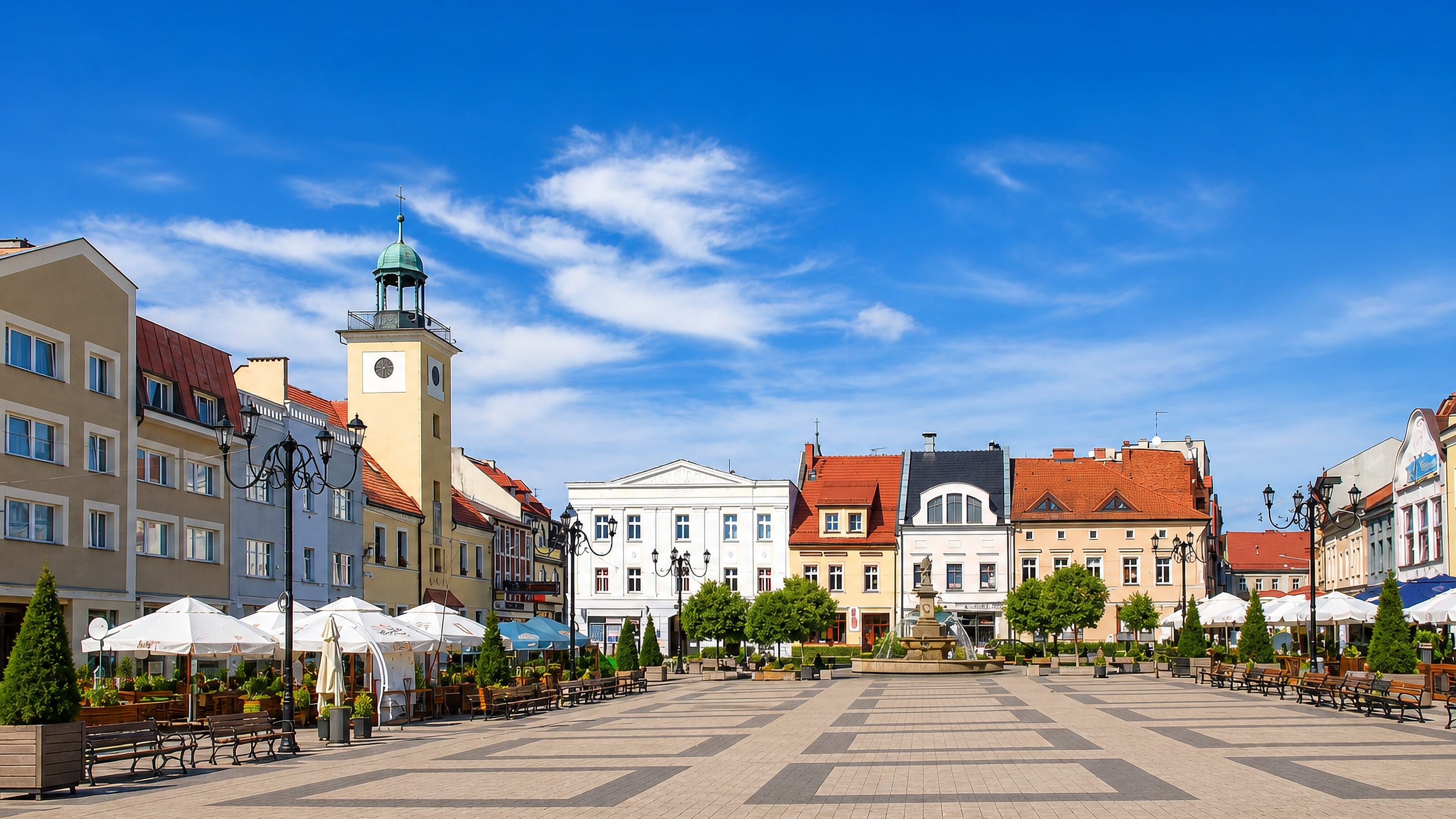 Rybnik market square, Poland, with the town hall clock tower, fountain and cafe umbrellas on patterned paving.