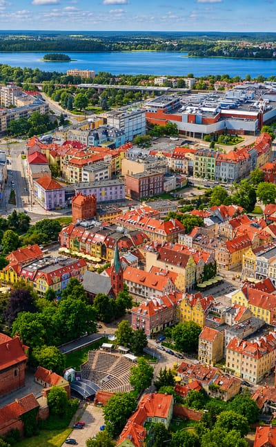 Aerial view of Olsztyn's Old Town, its red-brick castle and Gothic cathedral, with a Masurian lake beyond.
