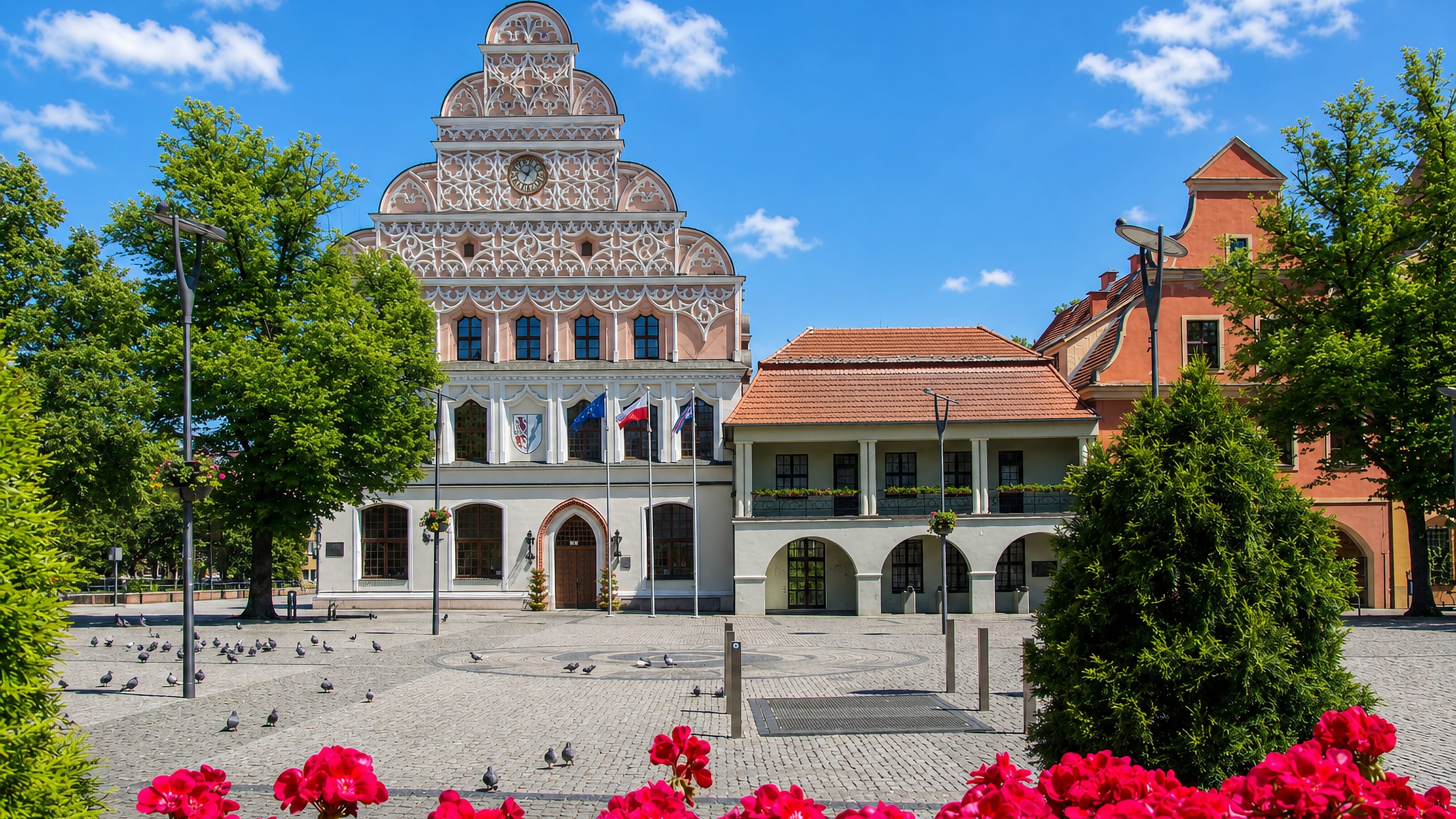 Stargard's ornate Gothic-gabled town hall on the Old Town Market Square, with flags, cobbles and red geraniums.