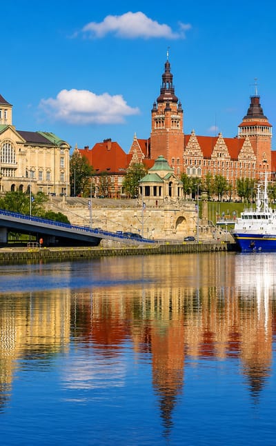 Szczecin's Chrobry Embankment and tower reflected in the Oder River, with boats moored below.