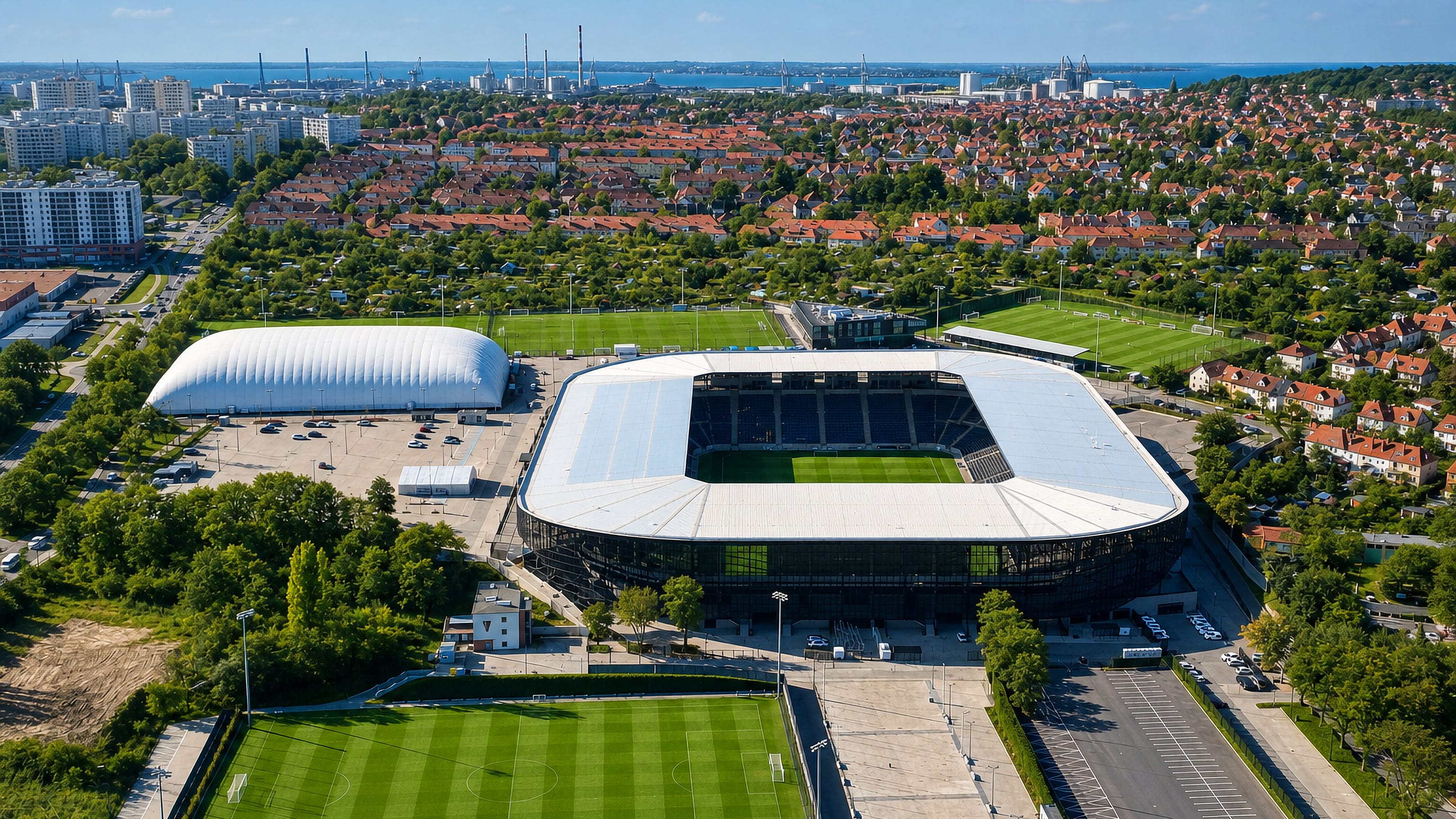 Aerial view of the Pogon stadium in Pogodno, Szczecin, amid red-roofed villas with the harbour beyond