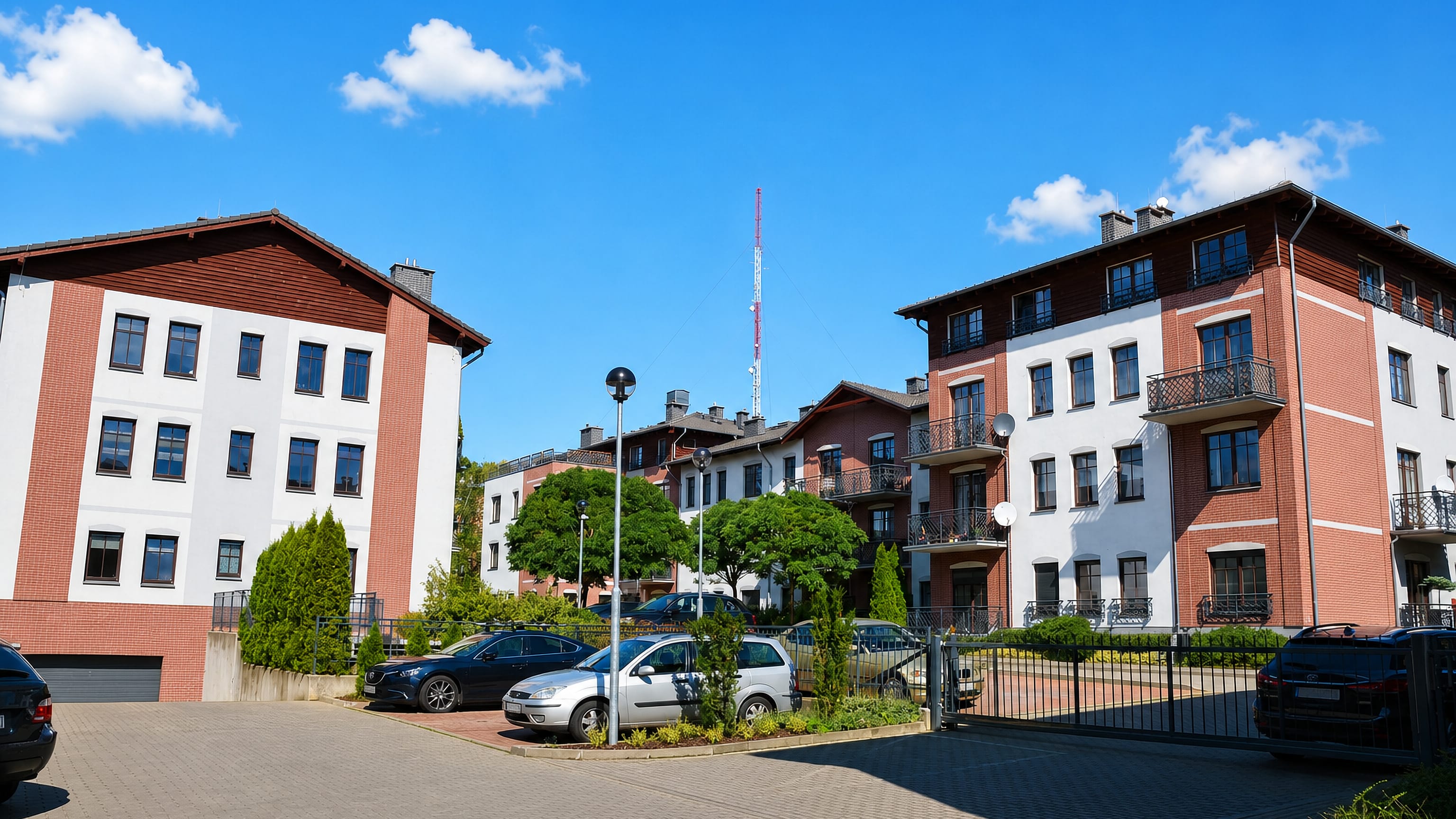 Red-brick and white apartment houses around a paved courtyard in Warszewo, Szczecin, below a mast.