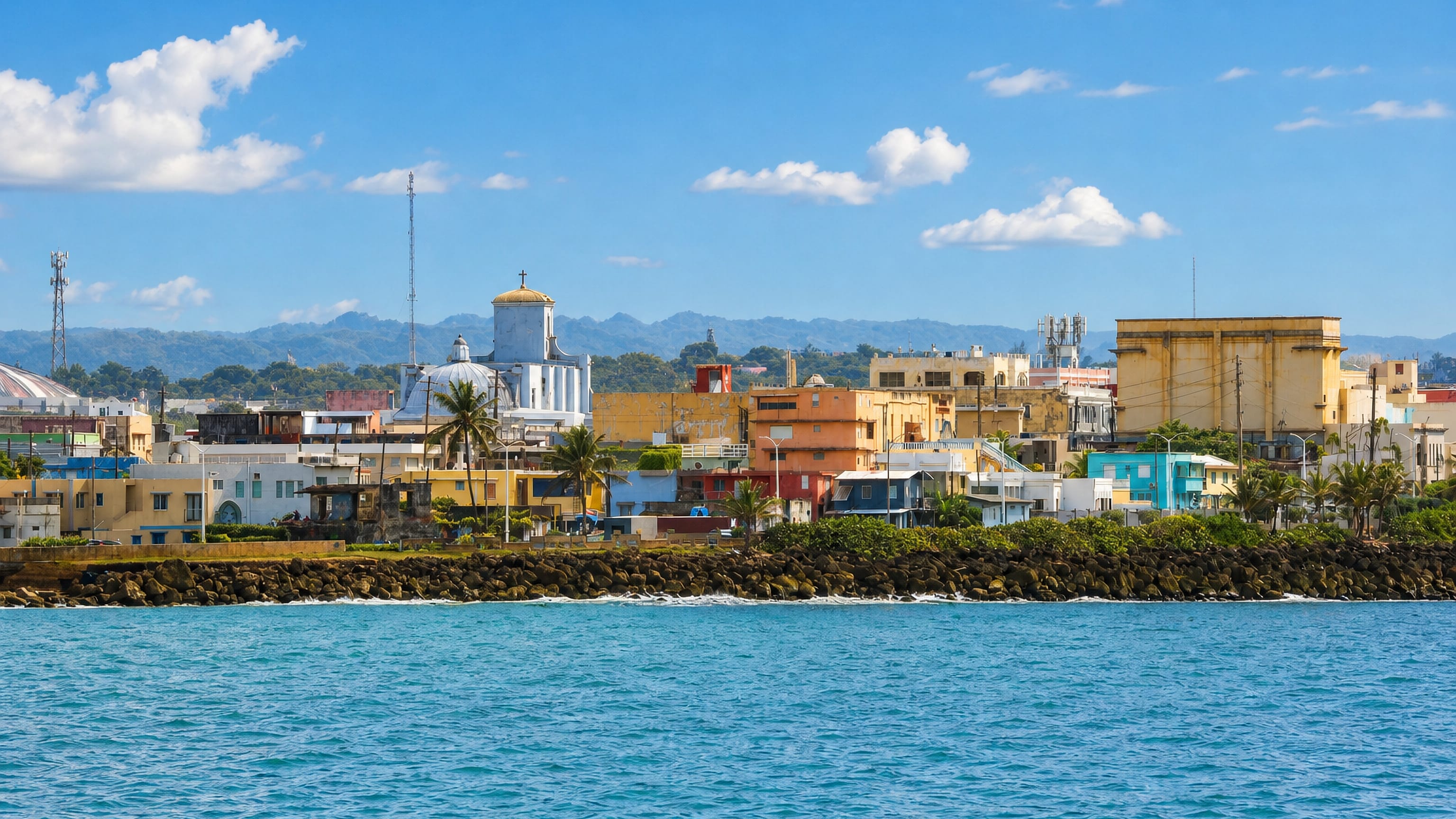 Arecibo, Puerto Rico, seen from the sea: its domed church and pastel buildings above a rocky shoreline.
