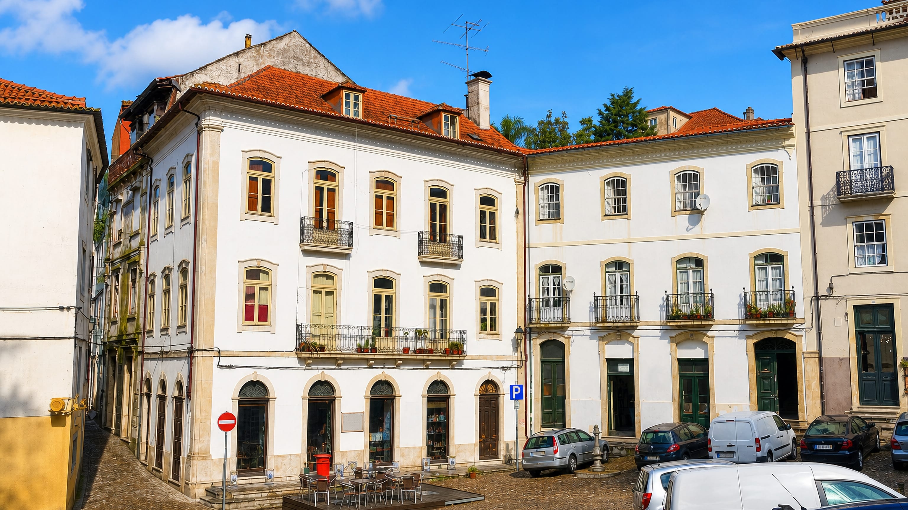 Cobbled square framed by white townhouses with wrought-iron balconies and a cafe terrace in Coimbra.