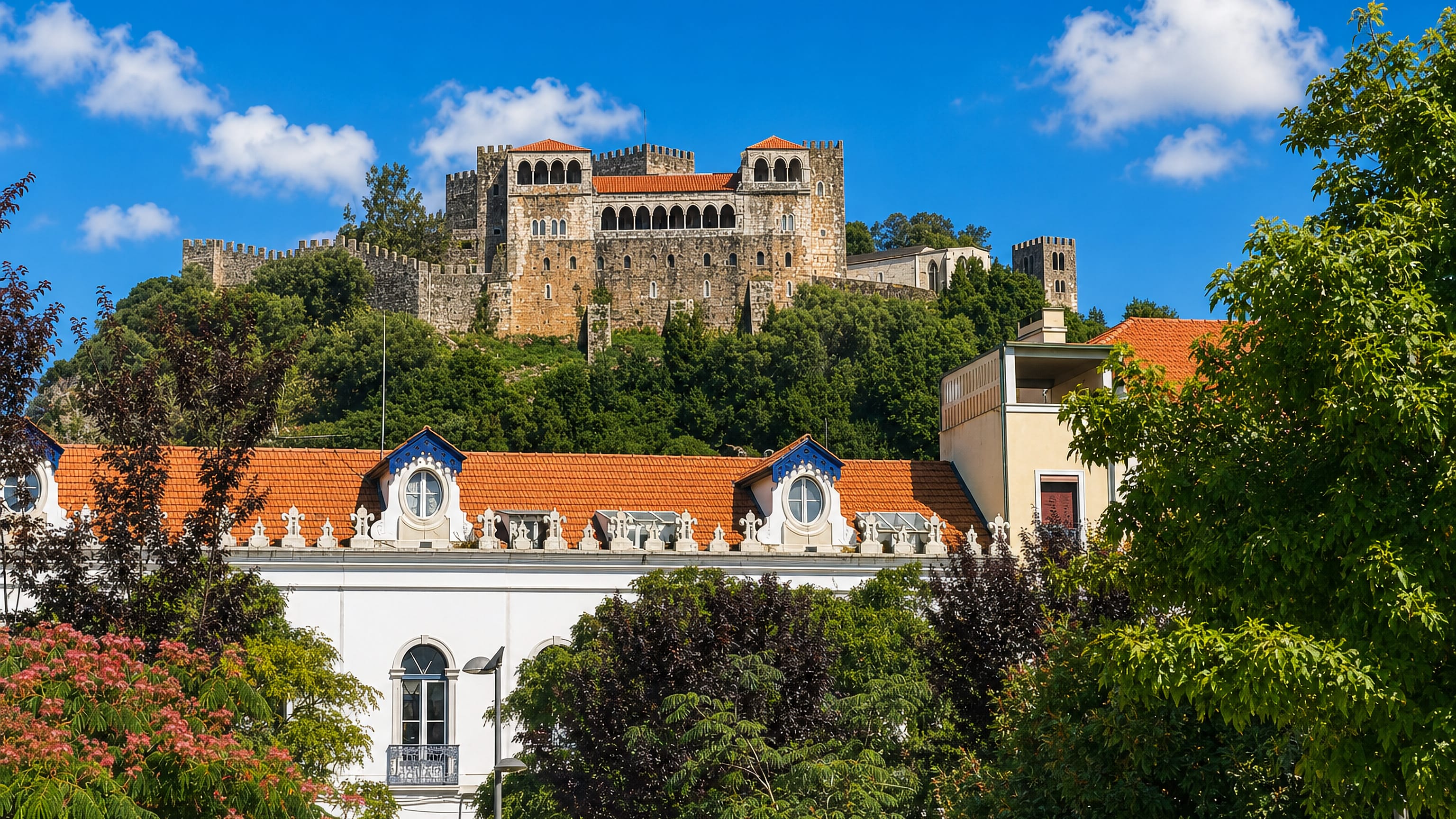 Leiria Castle with its arcaded loggia on the wooded hilltop above the terracotta rooftops of Leiria, Portugal