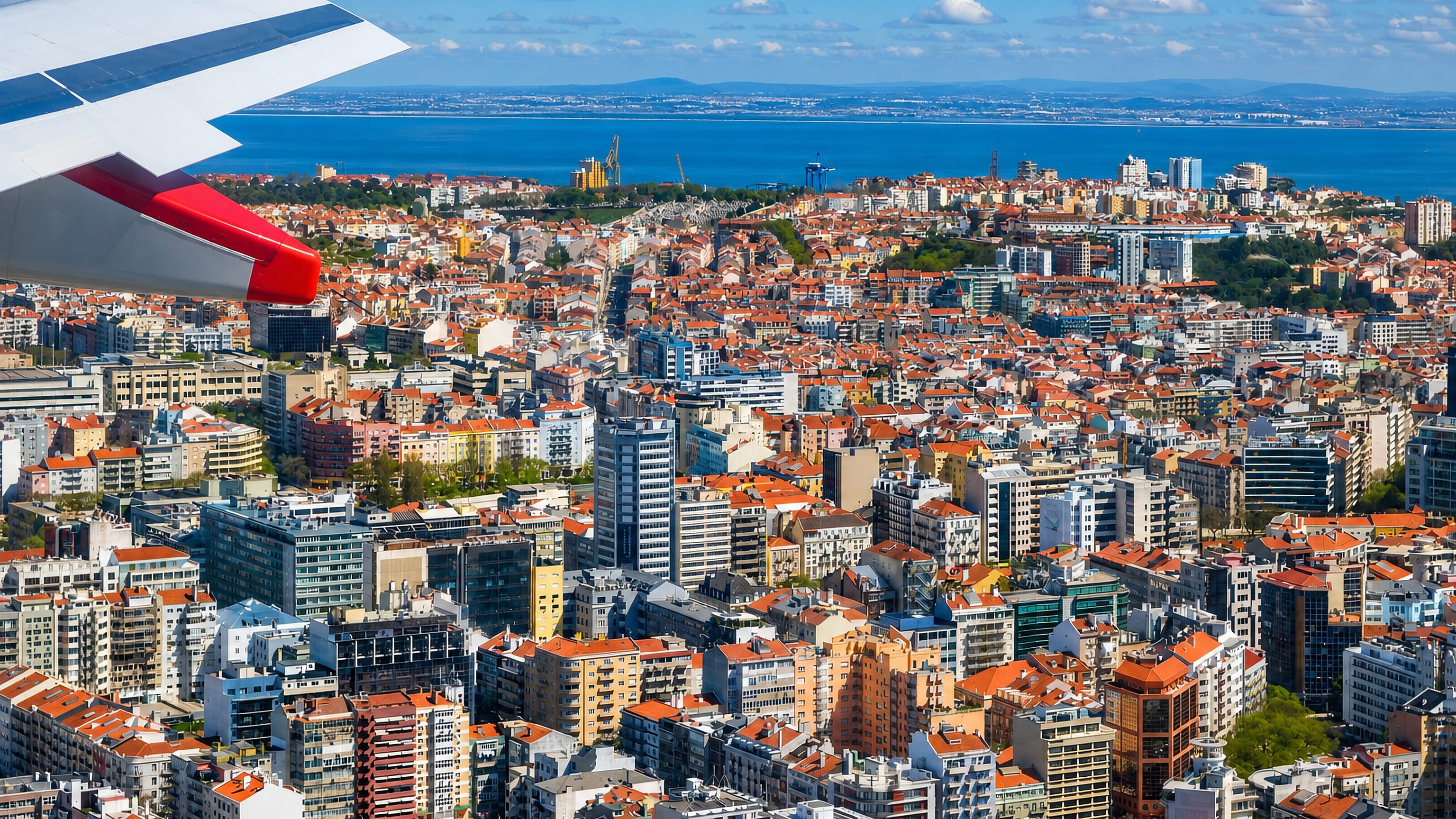 Aerial view over Avenidas Novas, Lisbon, of dense red-tiled rooftops reaching to the Tagus estuary.