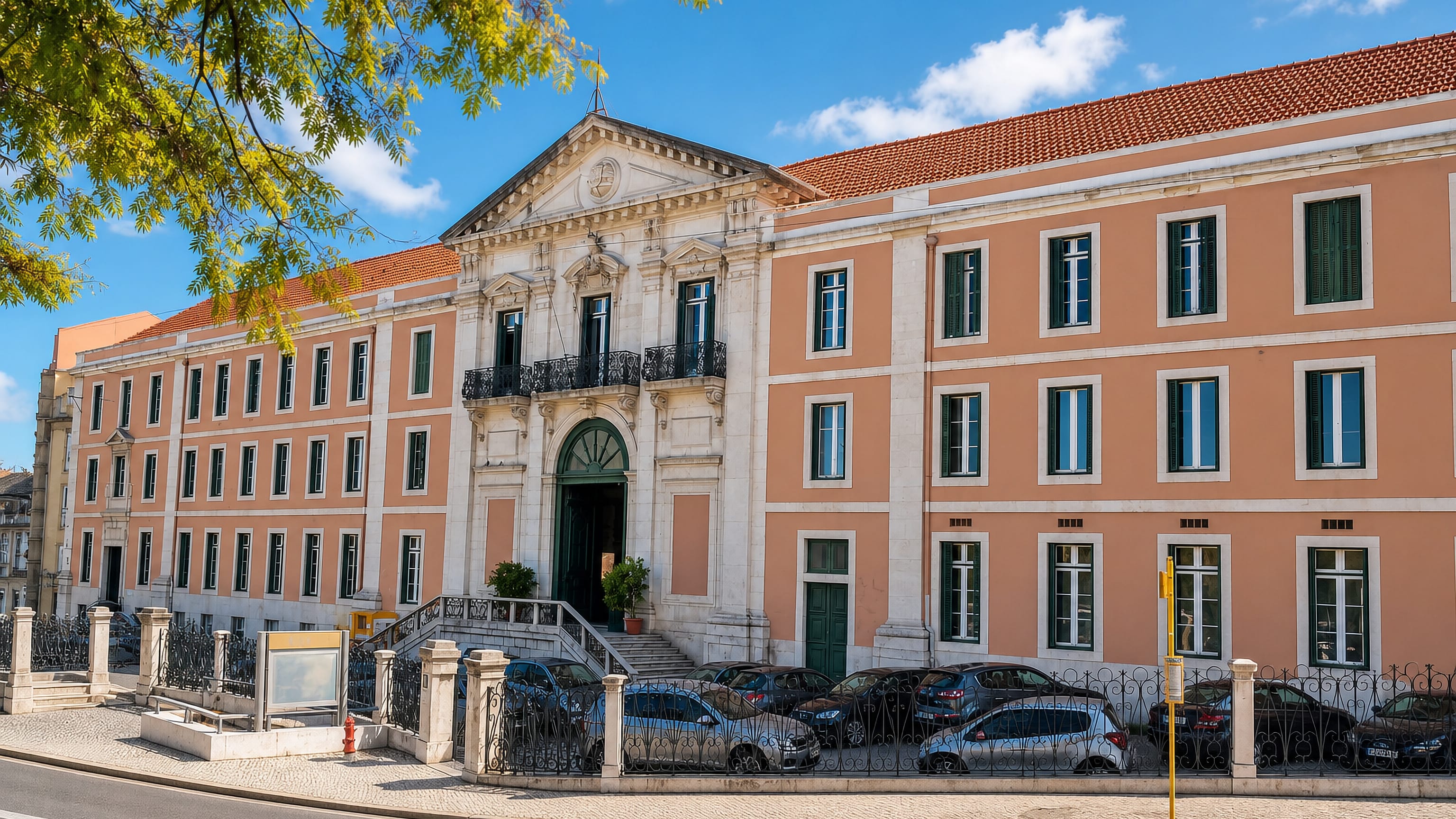 Salmon-pink neoclassical building with iron balconies on a calçada-paved street in Campo de Ourique, Lisbon.