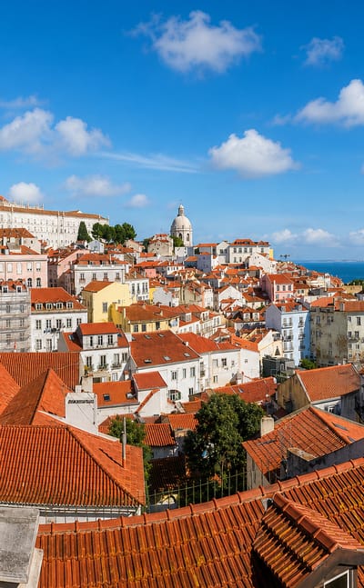 Lisbon's Alfama rooftops with the Sao Vicente monastery and National Pantheon dome above the Tagus River.
