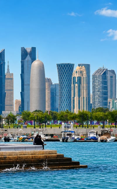 Doha's West Bay skyline of glass towers rising beyond a marina of moored boats along the Corniche.